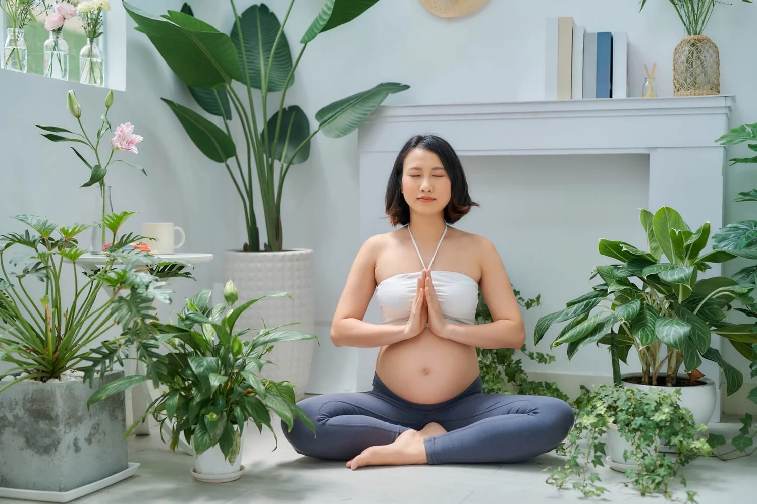 A pregnant woman meditating surrounded by plants.