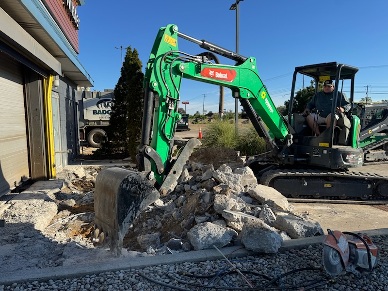 Excavator breaking out old concrete to prepare a commercial foundation site
