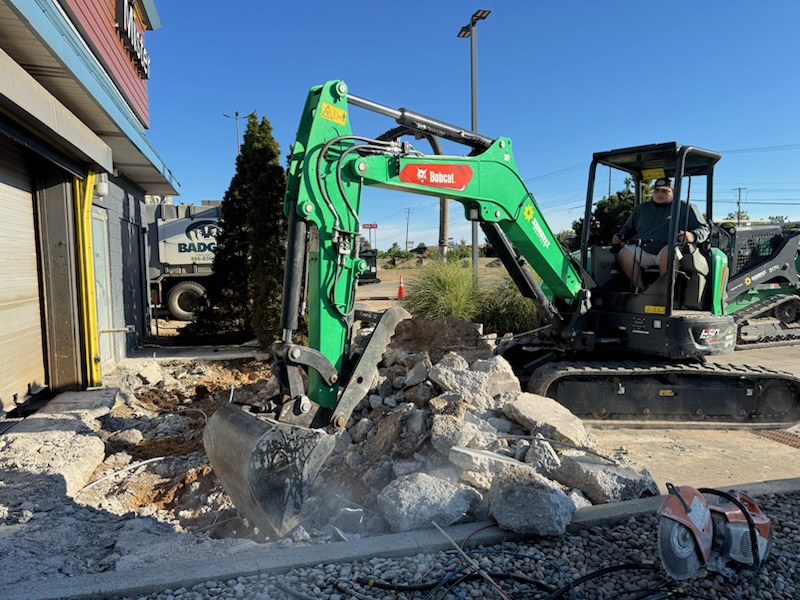 Excavator removing old concrete during site preparation for a custom concrete project in Holland, MI.