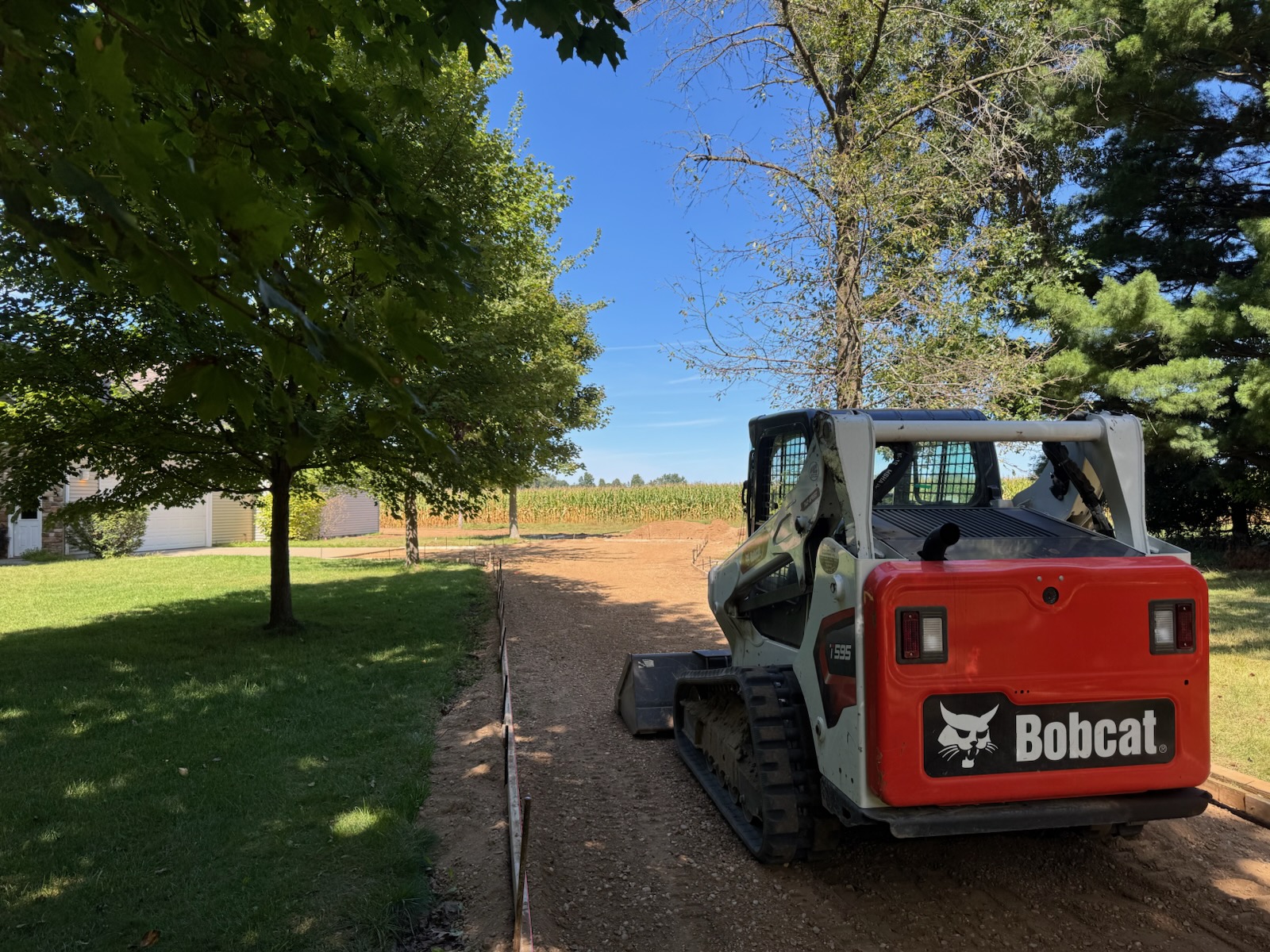 Skid steer grading a residential driveway base before a concrete pour