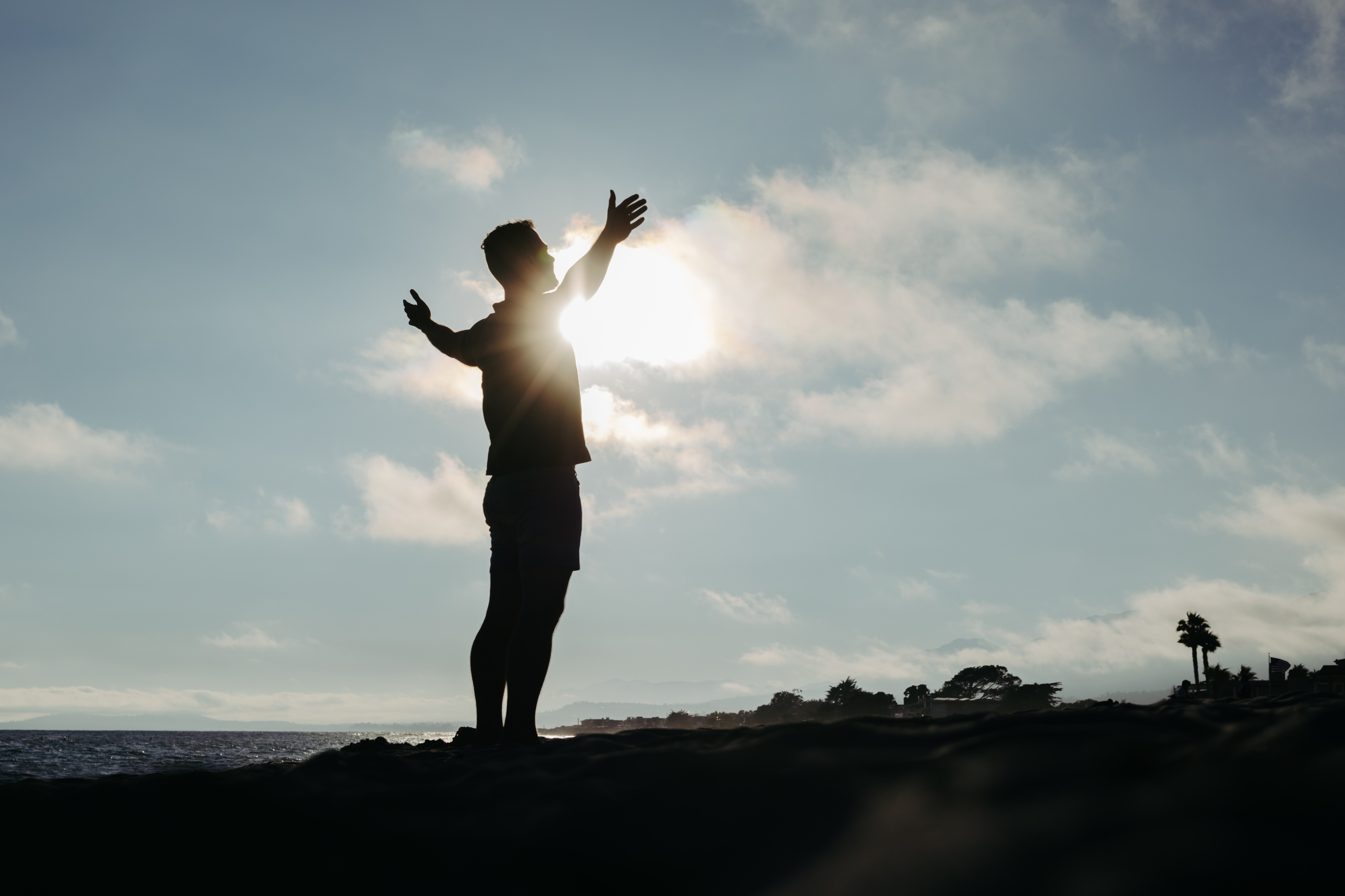 Jon Pinney silhouetted against the sun on a beach, standing with his arms open toward the sky.