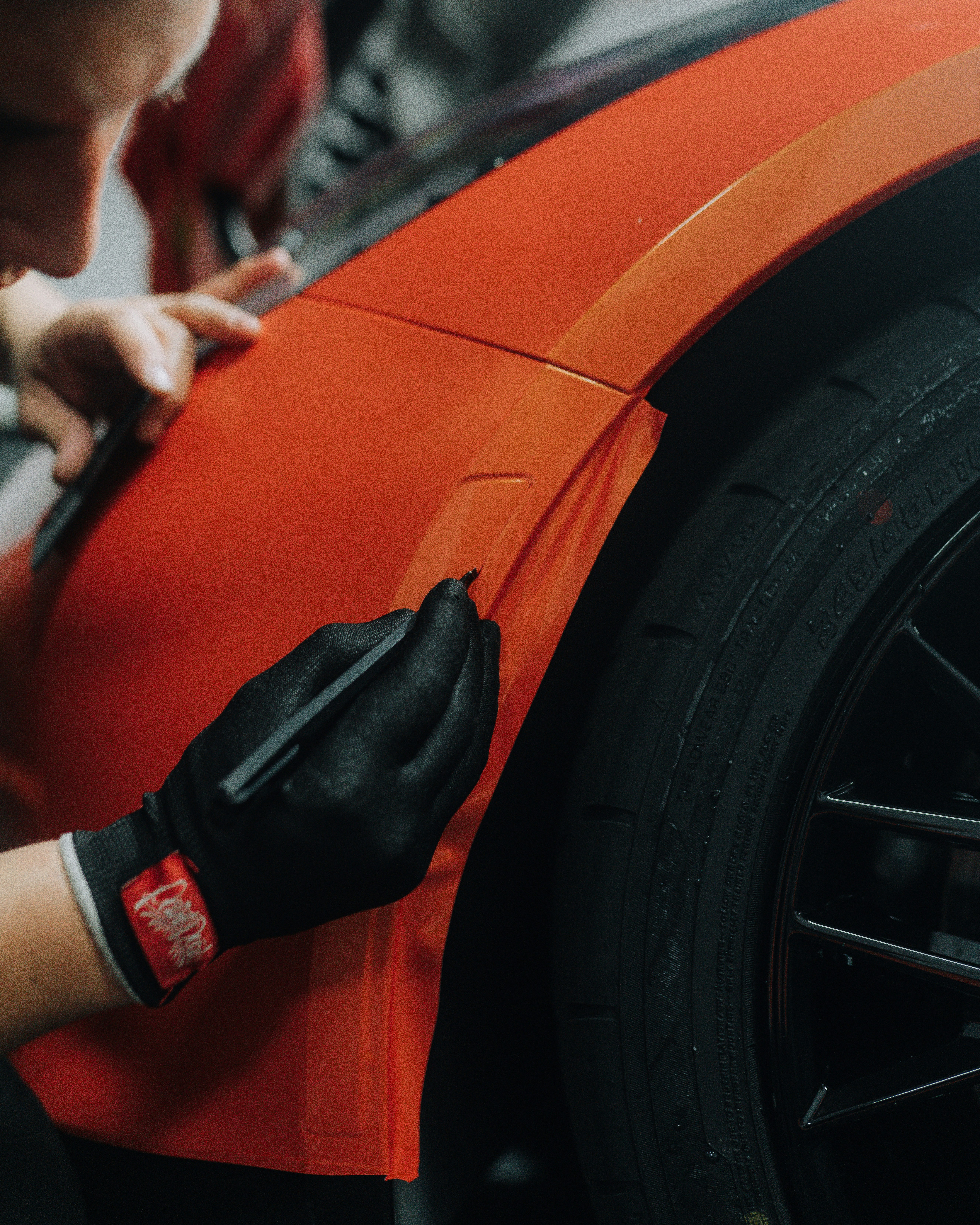 Orange vinyl wrap being squeegeed onto a car fender