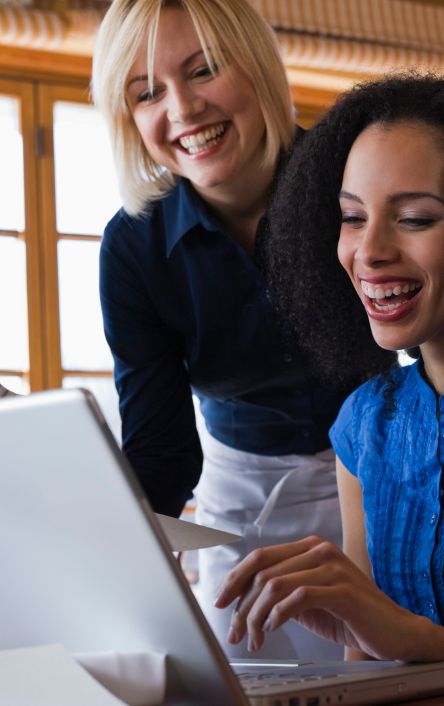 Two women looking over a laptop smiling