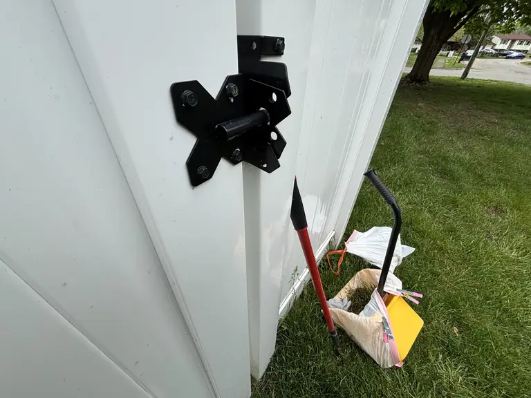 Closed white backyard gate with its black latch and cleanup tools.