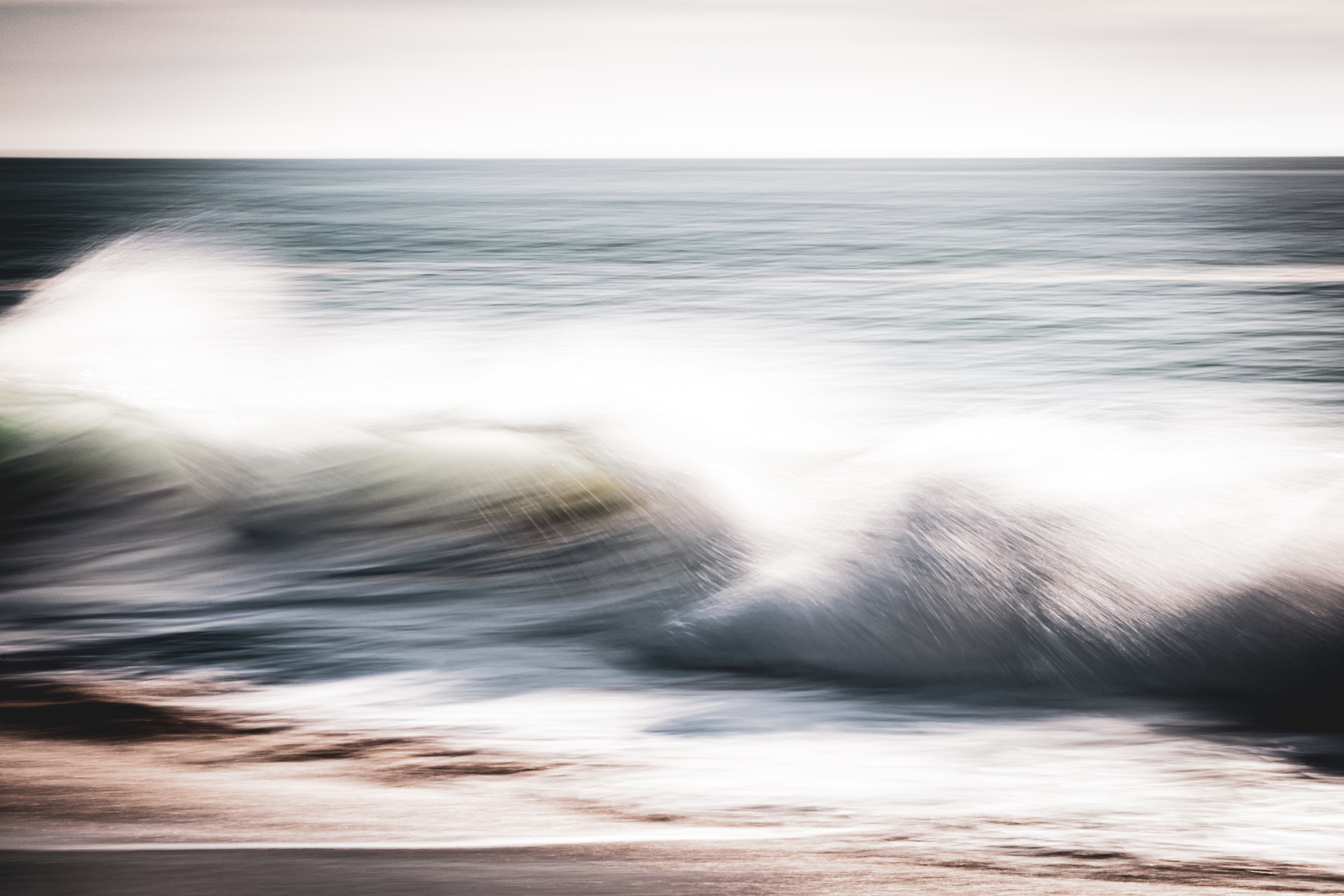 Long exposure ocean photograph of a wave breaking in radiant white light at Huntington Beach, California — motion blur and luminous spray captured with intentional camera movement. Part of the Coastal Blur series by Angie Harker. "The Winner Takes It All" — for Mum.