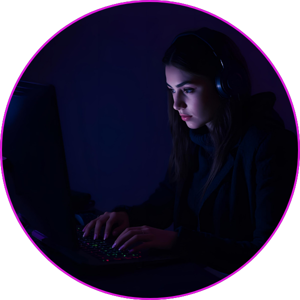 A woman wearing headphones works intently on a laptop in a dark room, illuminated by deep purple and blue lighting.