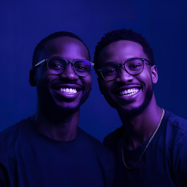 Two men wearing glasses smiling directly at the camera, illuminated with deep blue and purple lighting.
