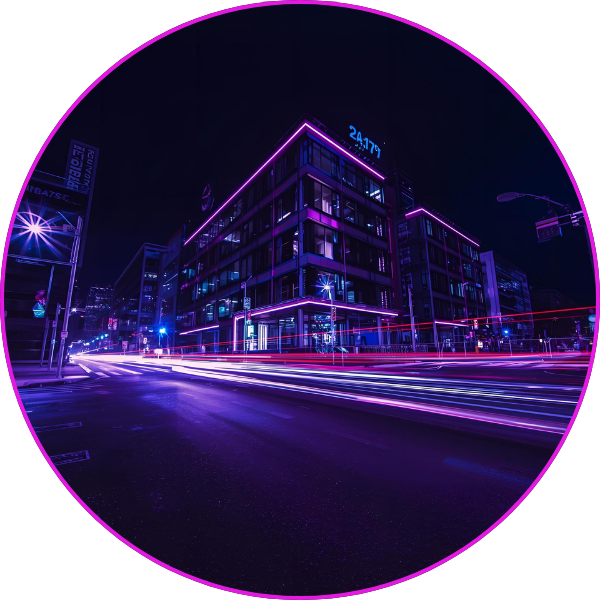 A nighttime cityscape with buildings outlined in purple neon lighting and long-exposure light trails from passing vehicles creating dynamic streaks across the street.