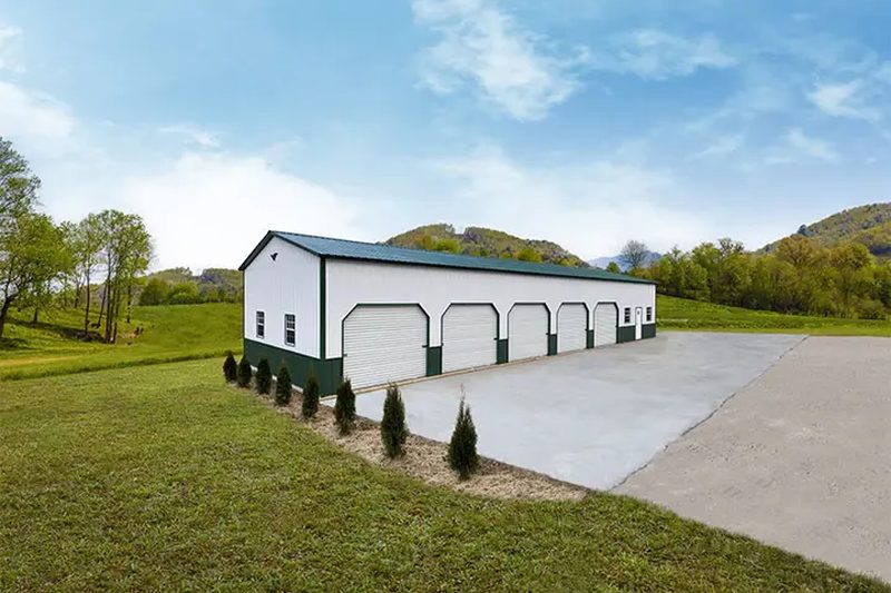 Long white and green commercial metal building with five roll-up bay doors and a concrete apron