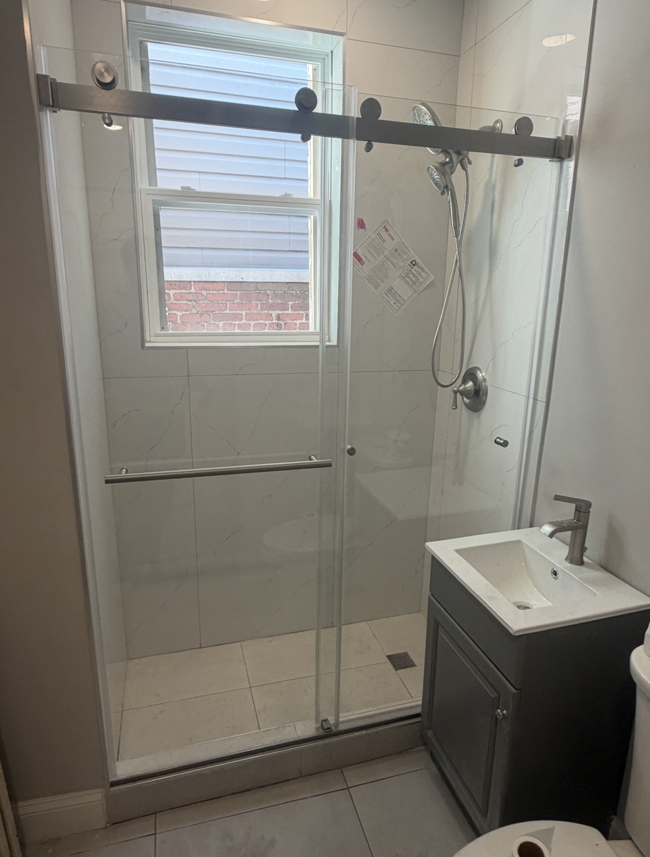 Frameless sliding glass shower door with black hardware in tiled bathroom