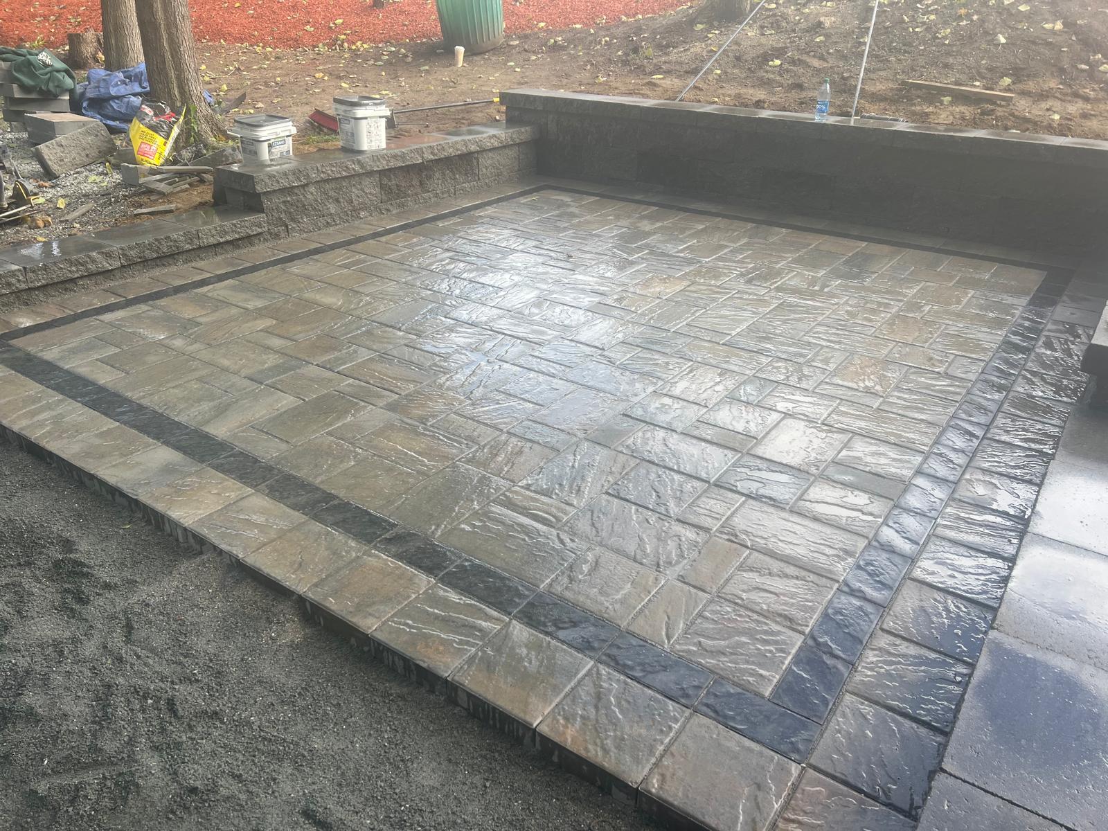 Expansive paver patio with geometric patterns, outdoor dining set, and decorative planters, set against a backdrop of a stylish suburban home.