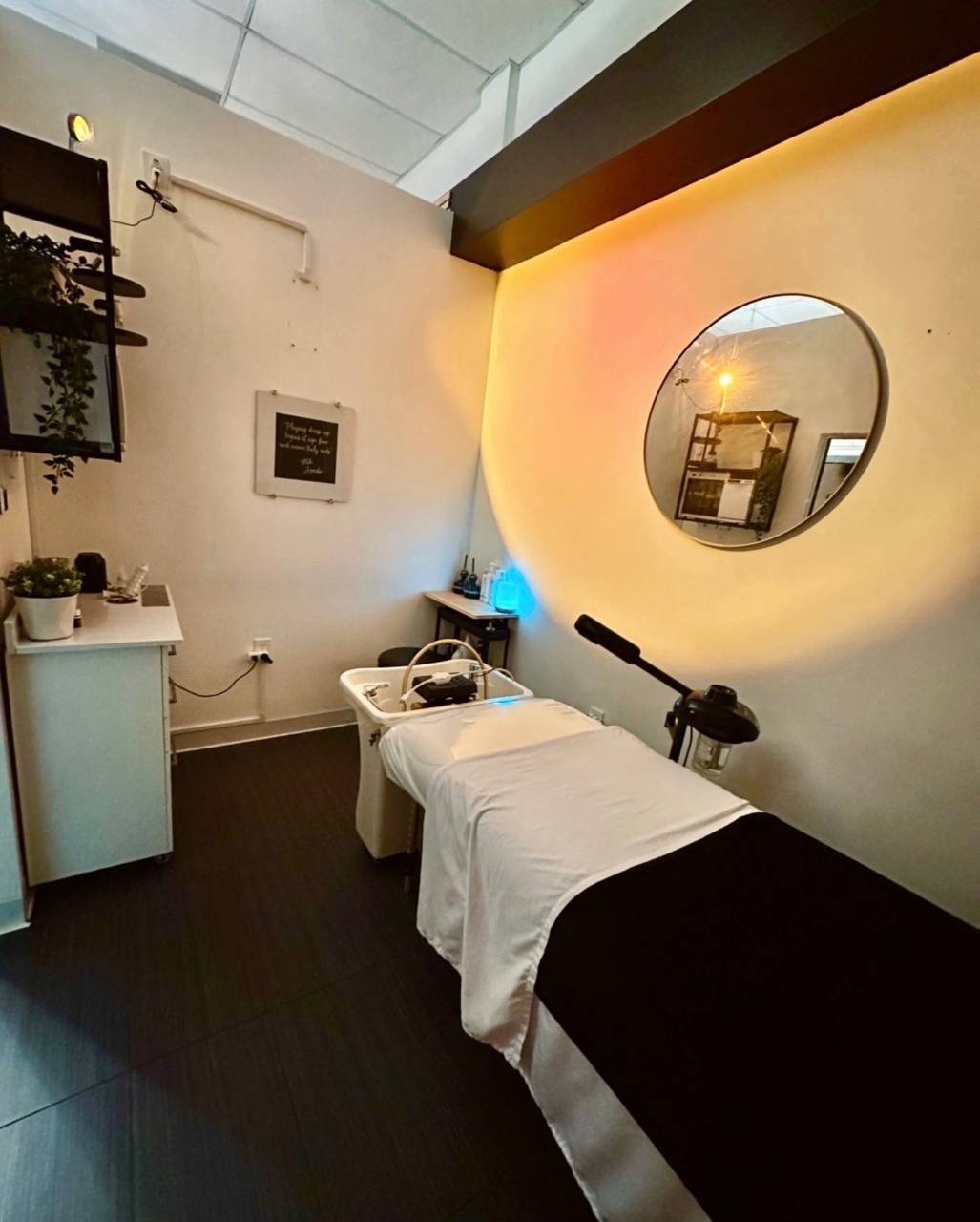 Treatment suite with large round mirror in golden glow, treatment bed, and plants