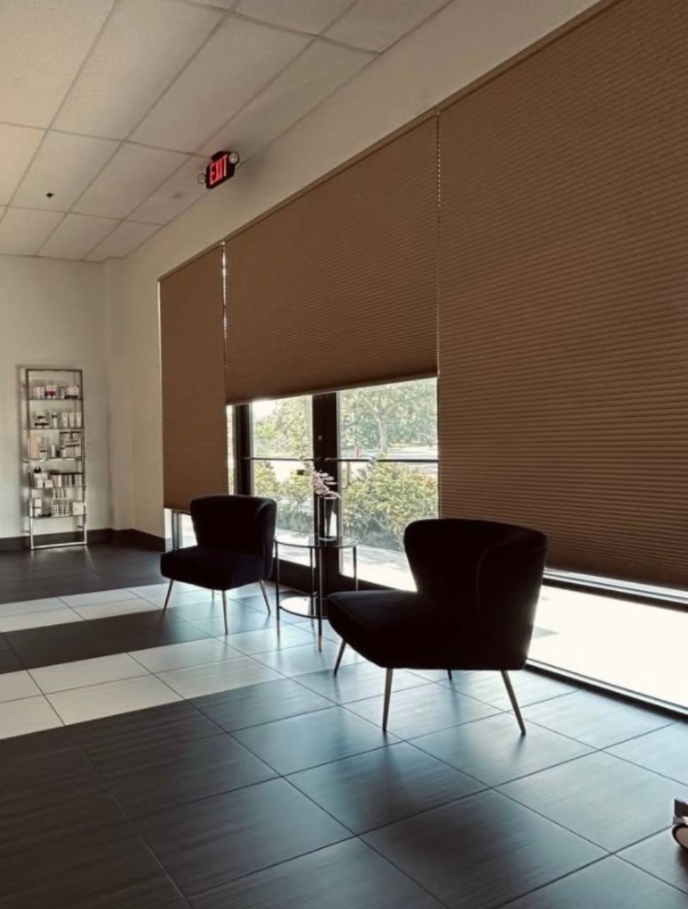 Client waiting lounge with dark velvet chairs, natural light, and retail product shelf
