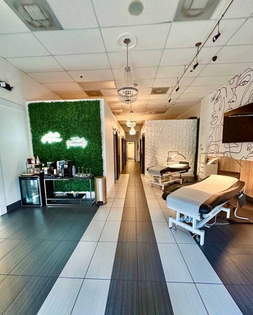 Hallway view of Your Signature Suites showing private suite doors, chandeliers, and the signature green wall with neon signs