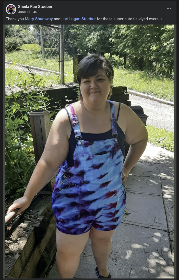 Person outdoors wearing bright blue, purple, and magenta handmade tie-dyed short overalls