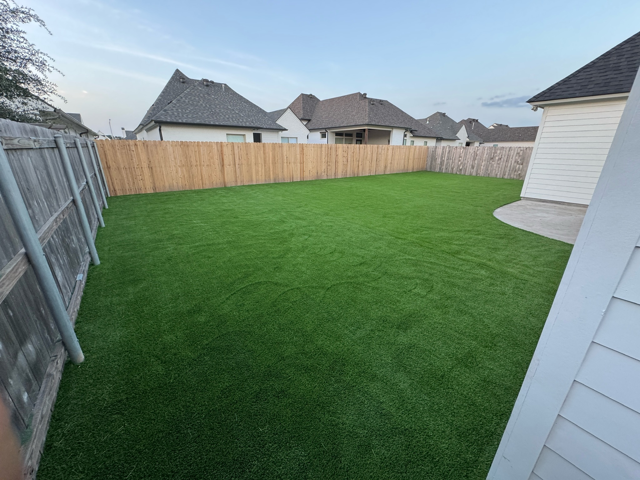 Artificial turf lawn with a curved edge beside a white home