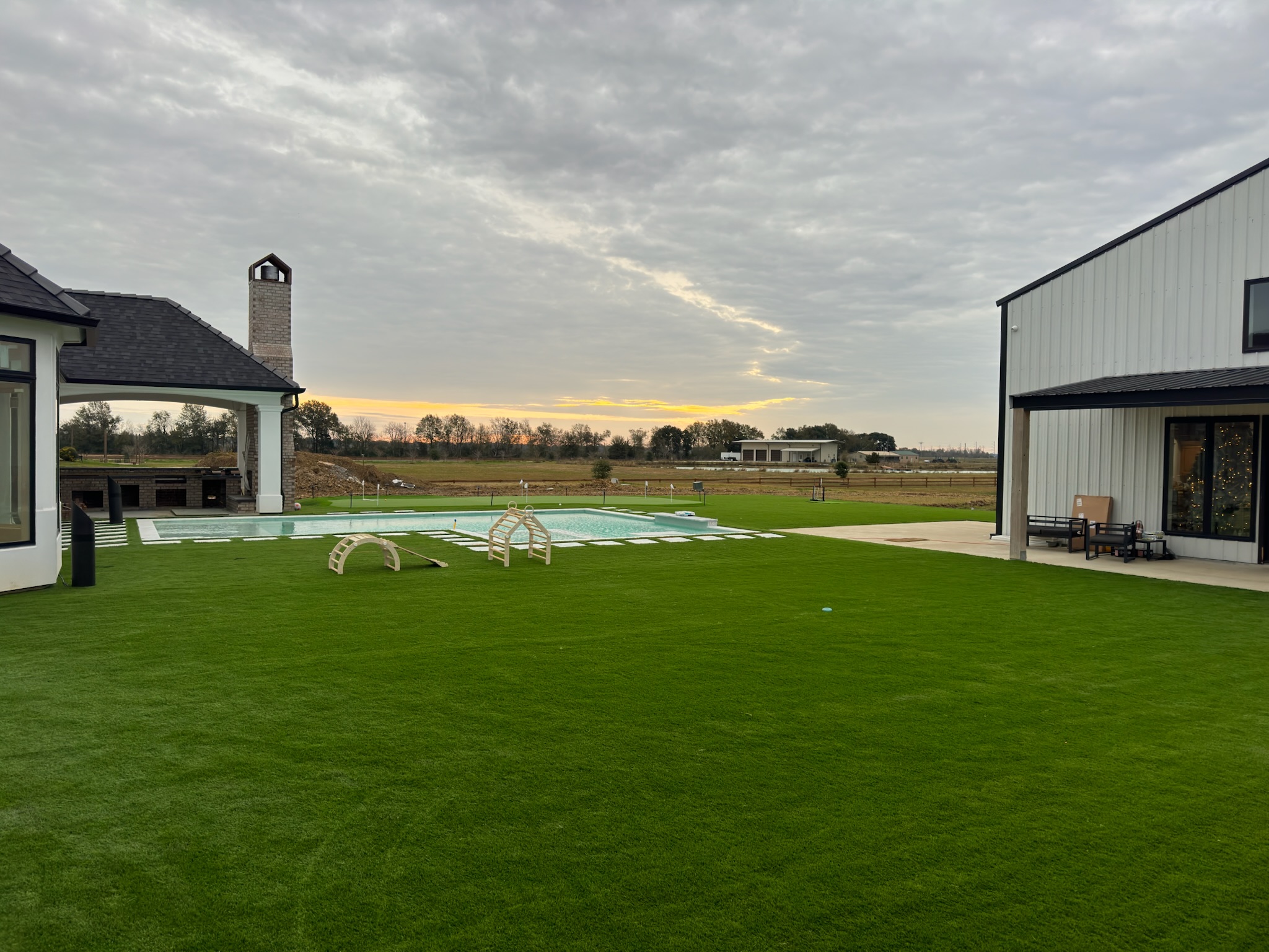Broad artificial turf lawn between a home and an outbuilding at sunset