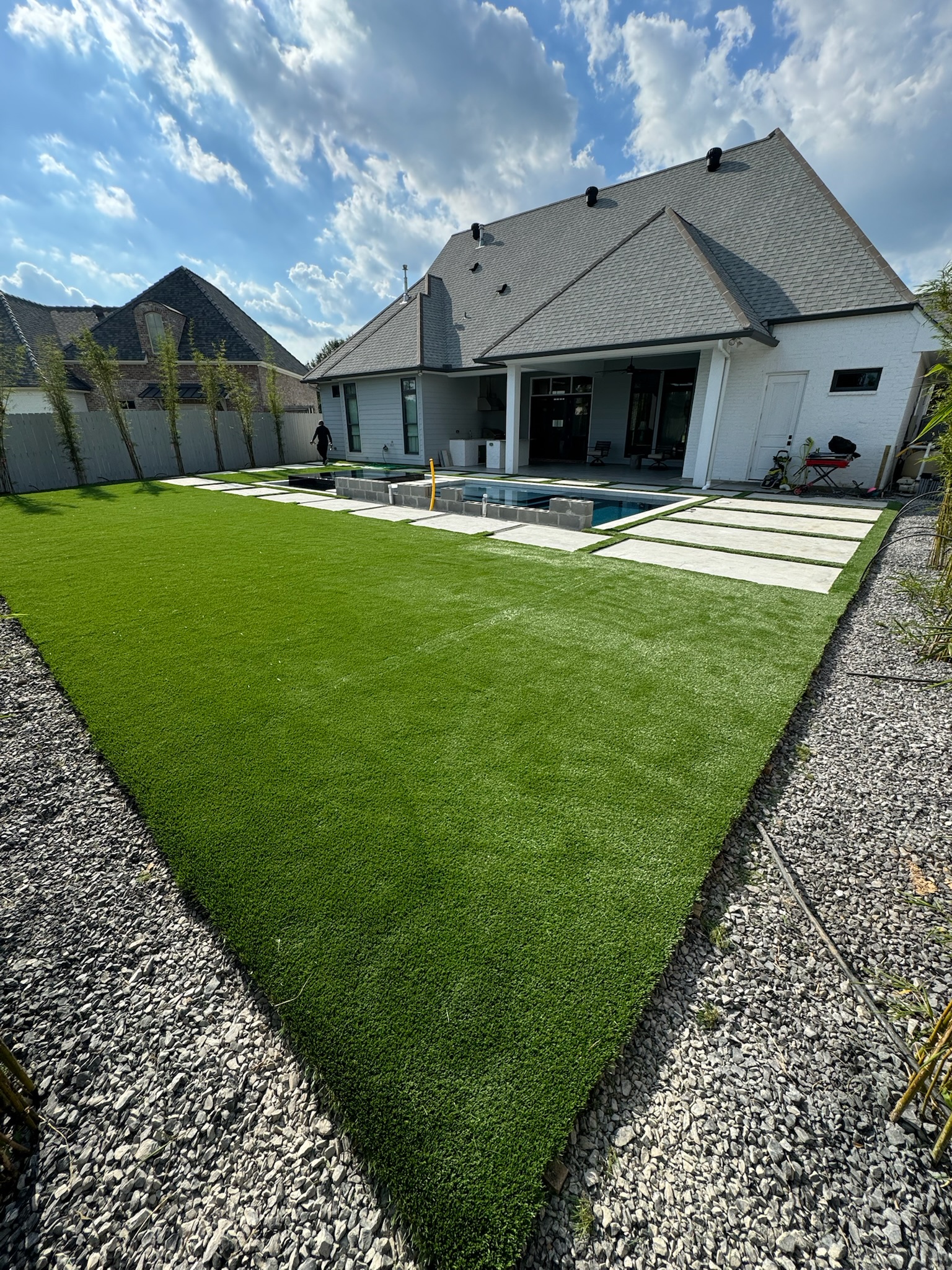 Residential turf lawn with a white home and covered patio in the background