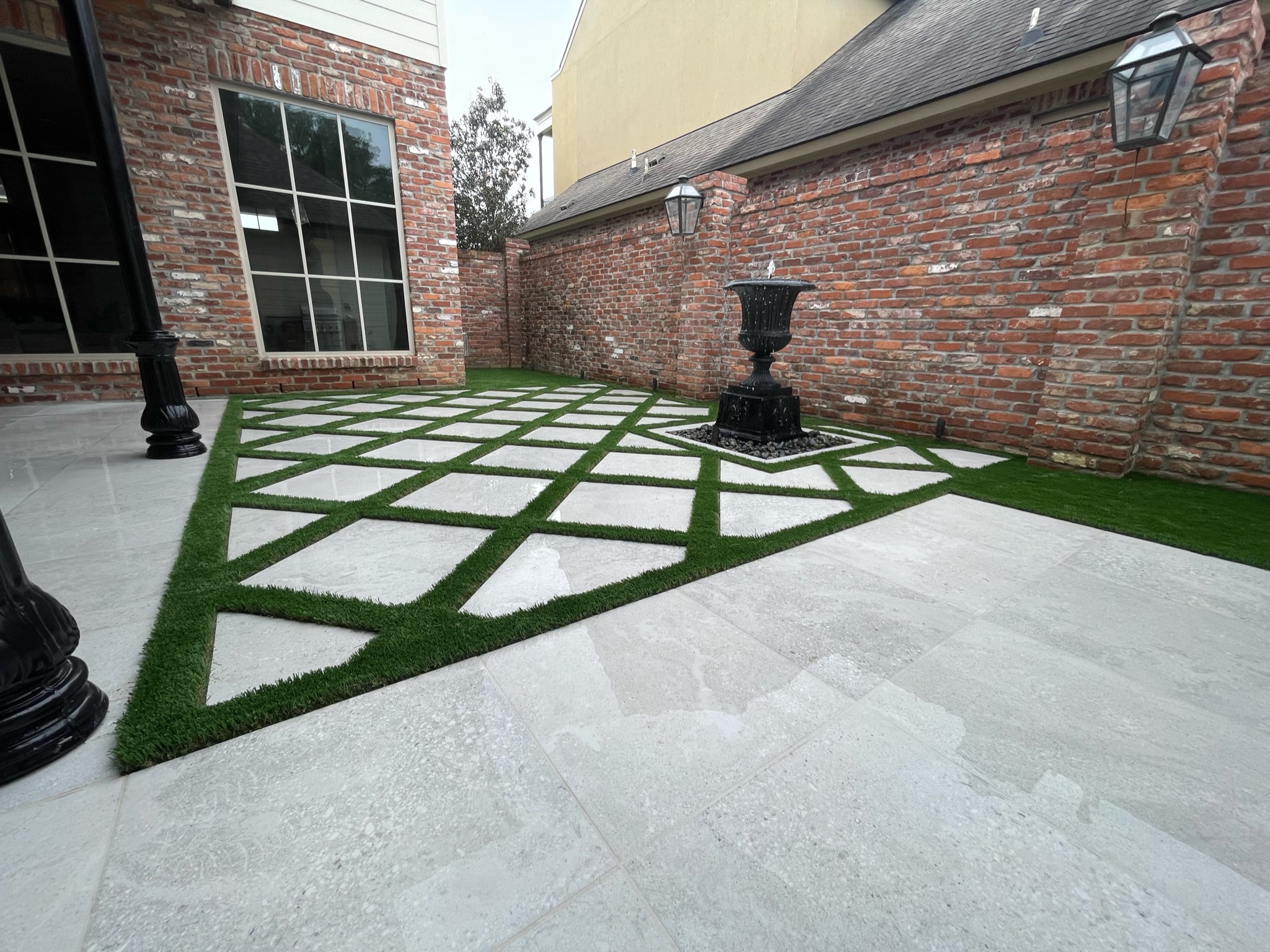 Geometric pavers separated by artificial turf in a brick courtyard