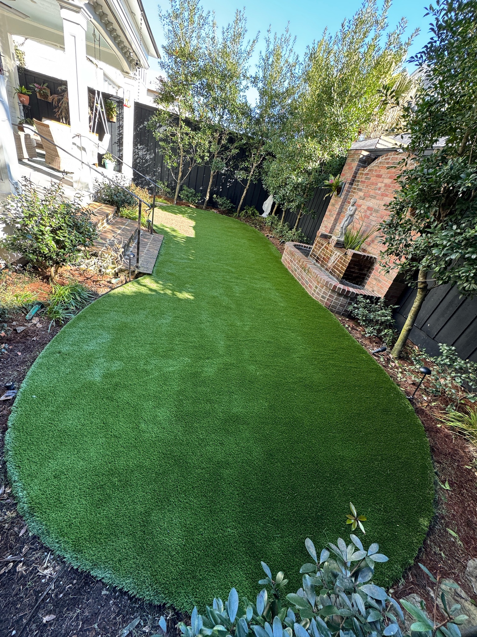 Narrow artificial turf side yard bordered by plants and a fence