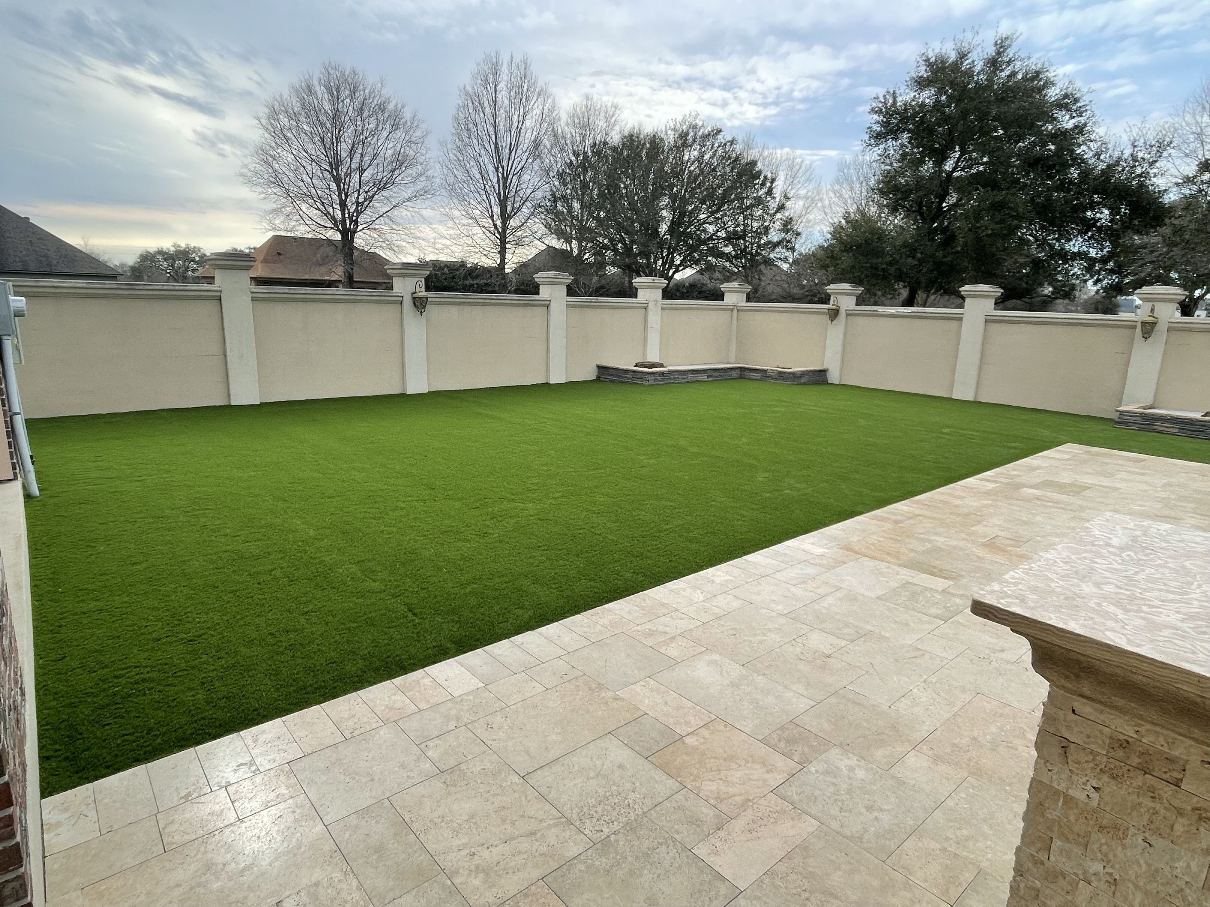 Finished rectangular turf backyard beside a paved patio and white fence