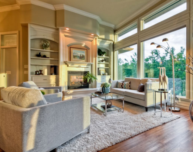 Bright staged living room with a fireplace, built-in shelves, neutral sofas, glass coffee table, plush rug, and large windows bringing in natural light.