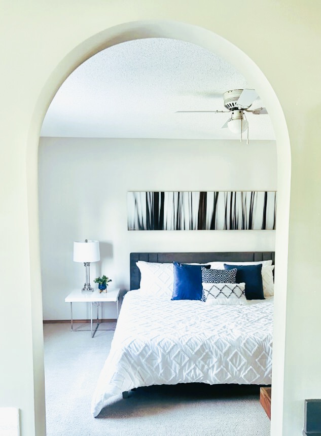 Staged bedroom with gray bed, white bedding, and blue accent pillows.