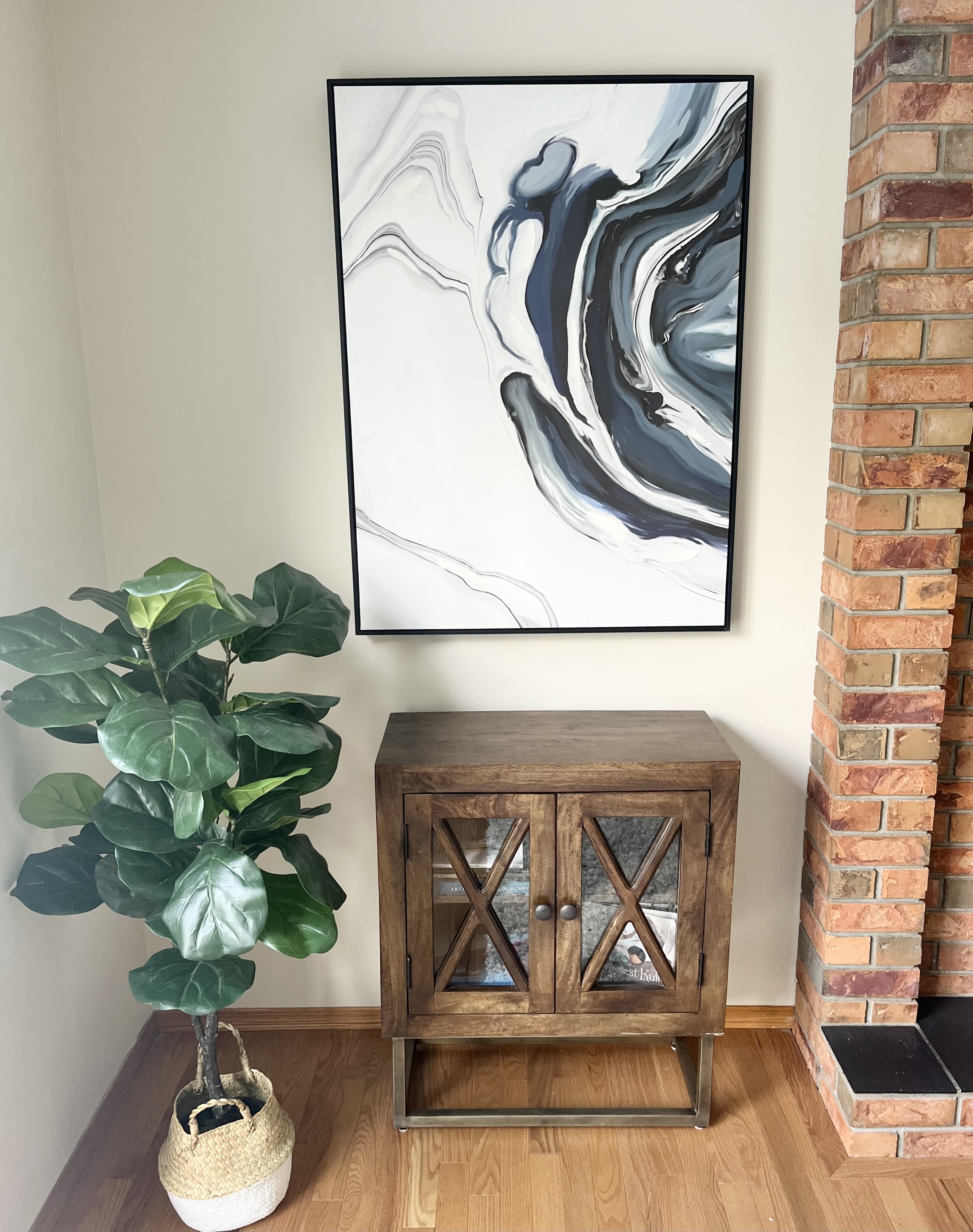 Staged living room corner with abstract wall art, wood cabinet, and potted plant.”