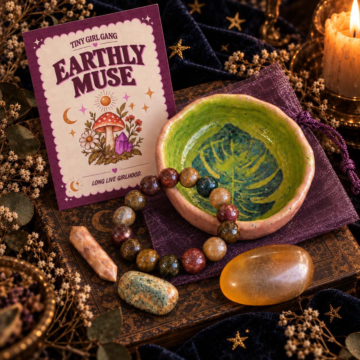 Curated Tiny Girl Gang treasures — crystals, ceramic bowl, beaded bracelet, and an Earthly Muse card arranged on a starry velvet cloth