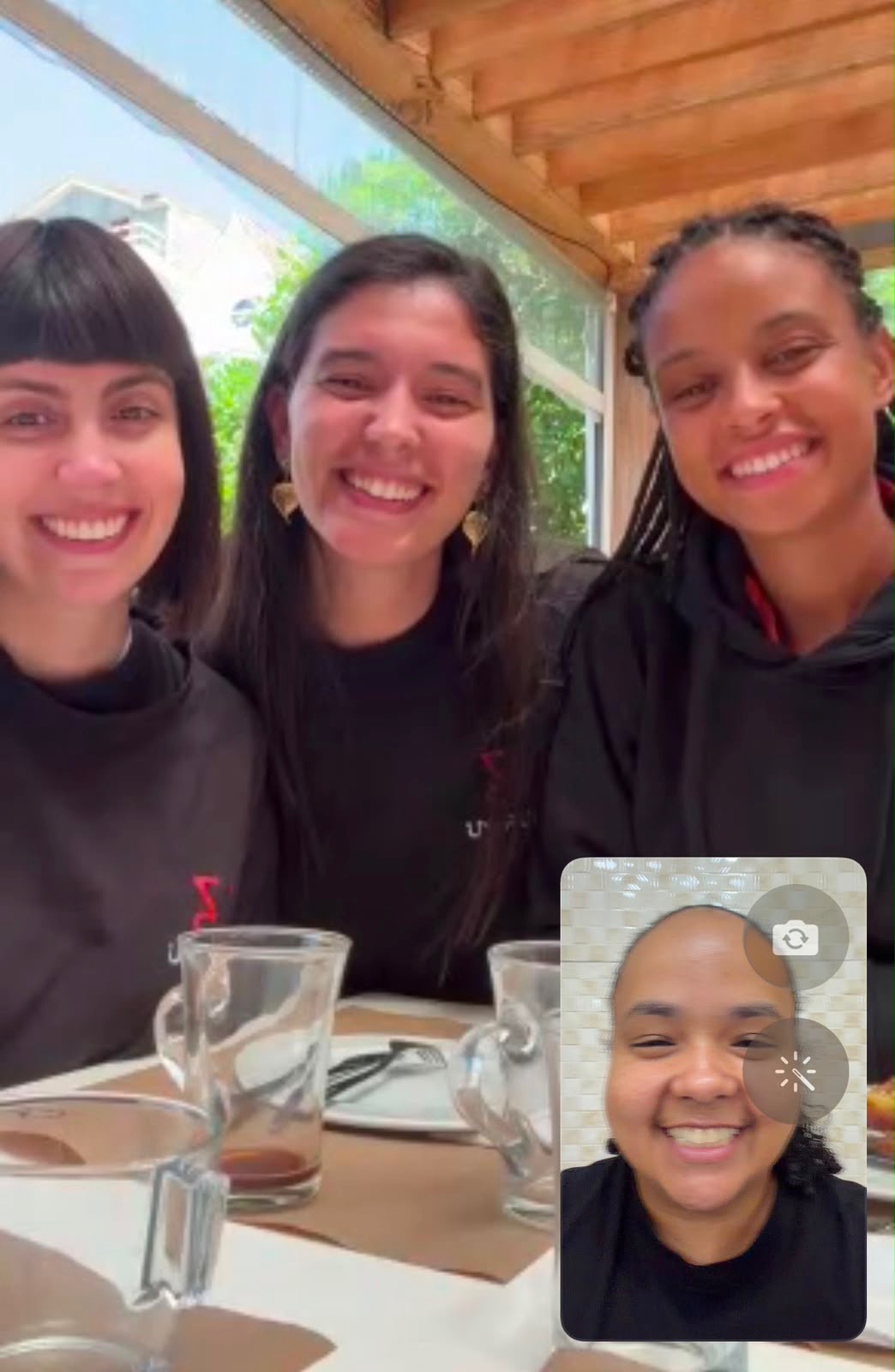 Três pessoas da equipa UNRULE a rir à mesa, com a quarta em videochamada no telemóvel
