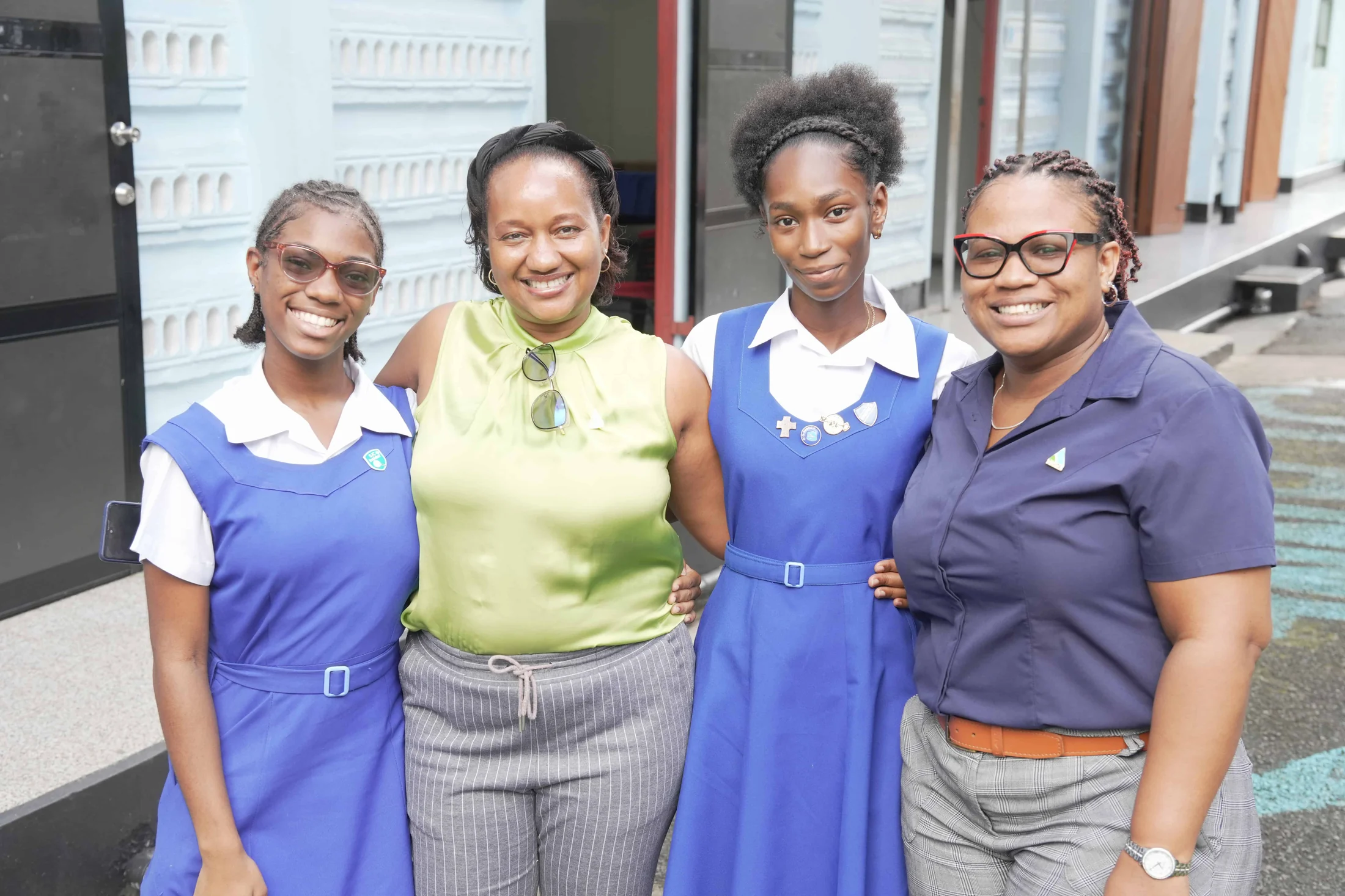 Two schoolgirls in blue uniforms stand with two women outside their school