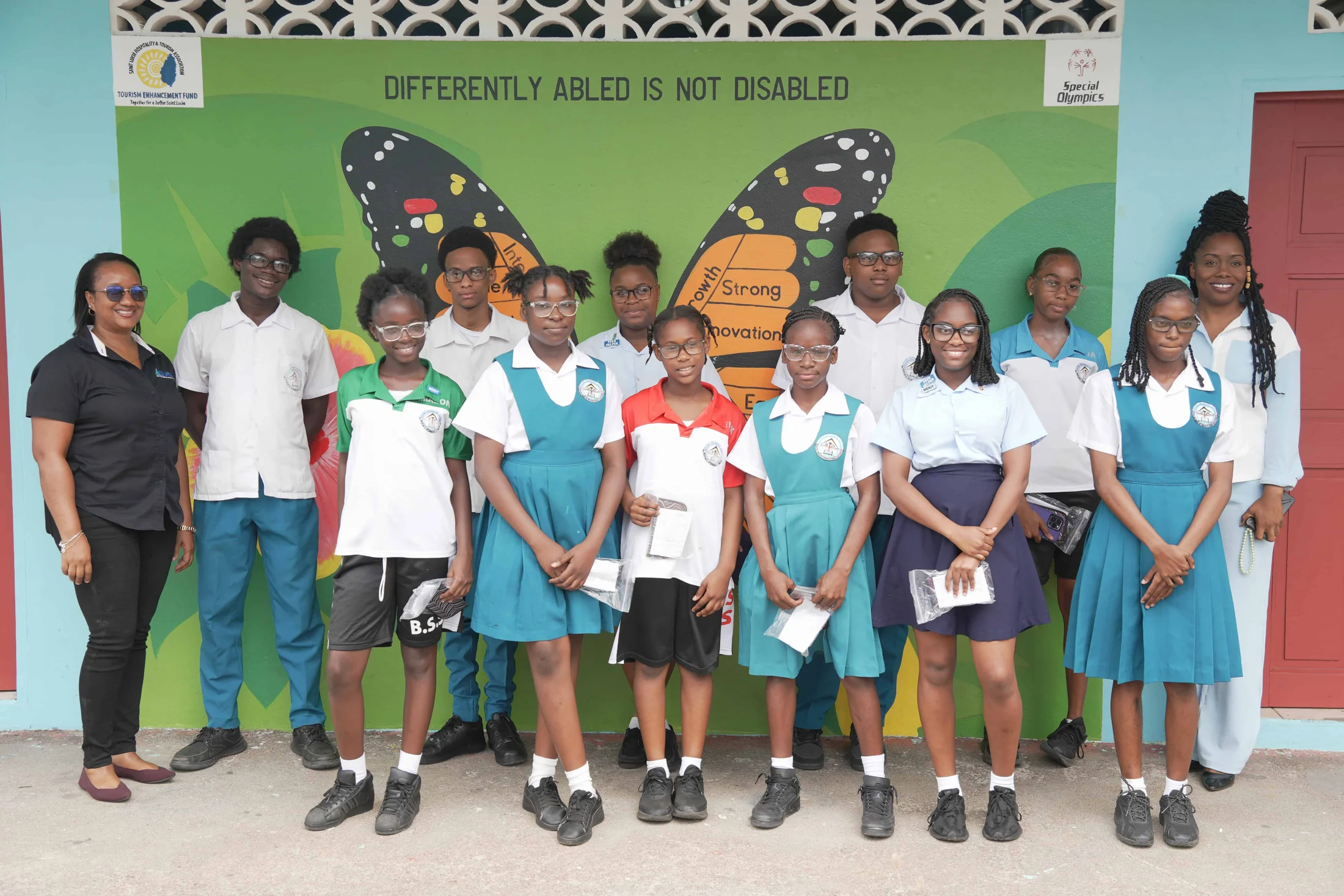 Students and teachers stand in front of a 'Differently abled is not disabled' butterfly mural