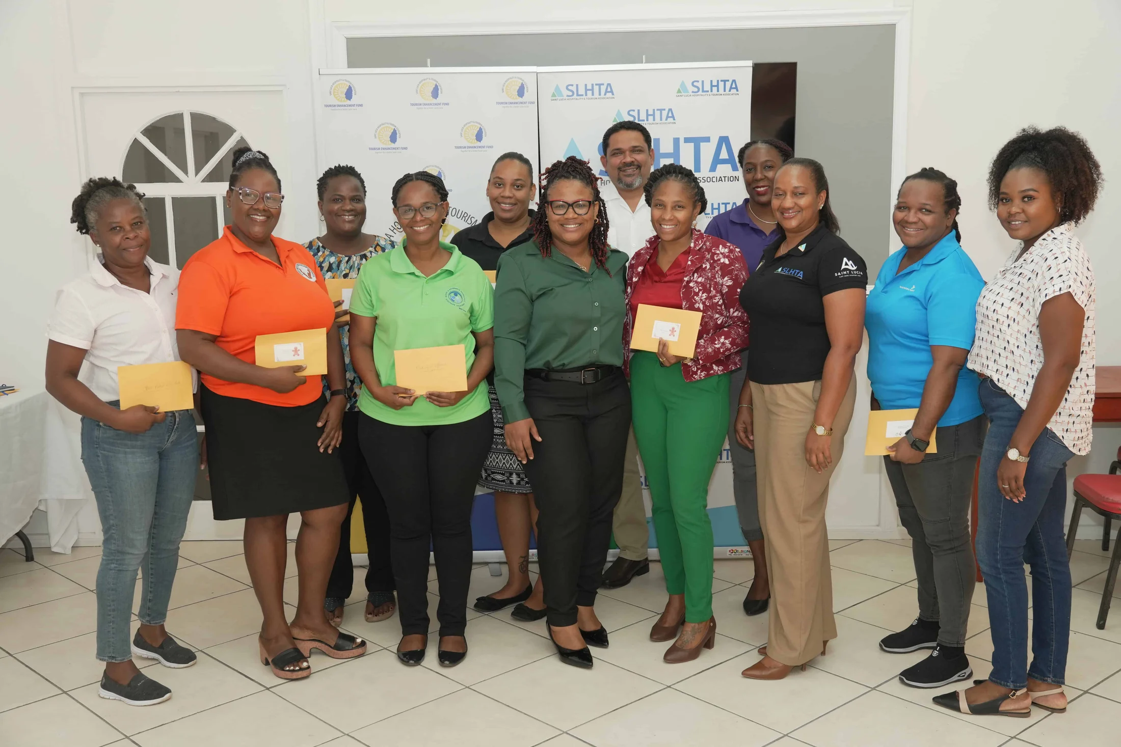 A group of grant recipients hold their envelopes with SLHTA staff