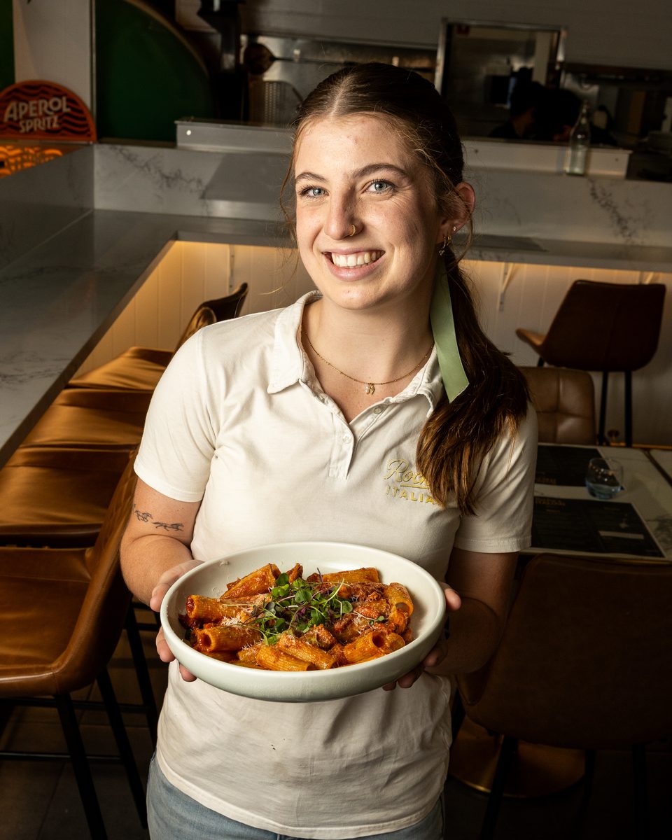 A Rocky's Italian team member holding a bowl of chicken and chorizo rigatoni