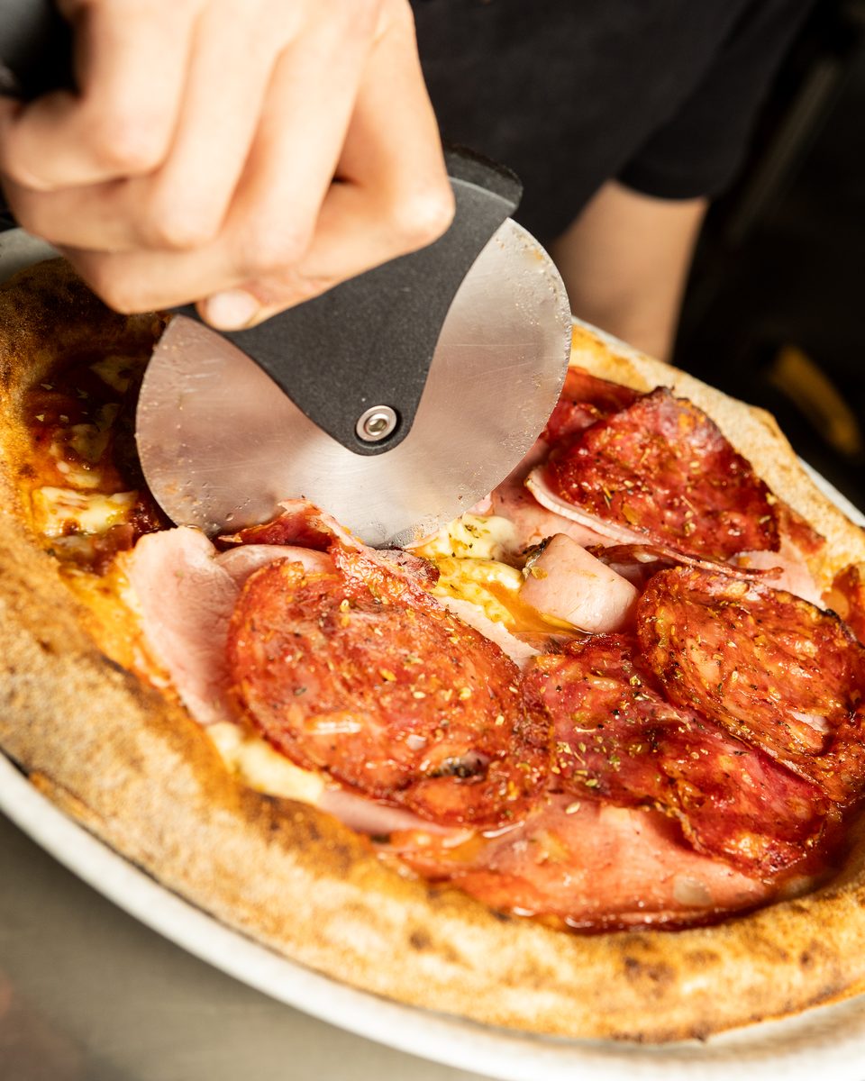 Meatlover Italia pizza being sliced with a pizza wheel