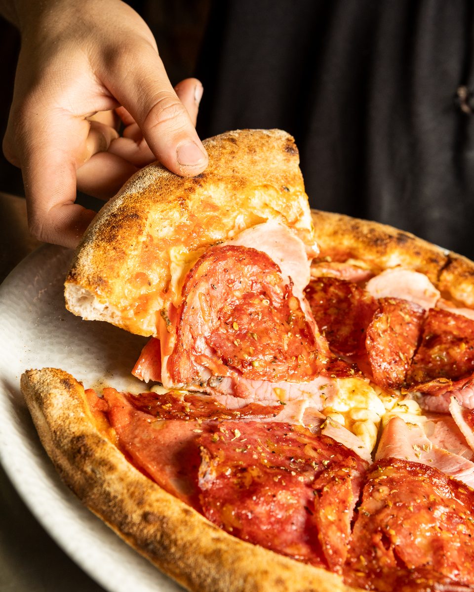 A slice of Meatlover Italia pizza lifted off the wood-fired base