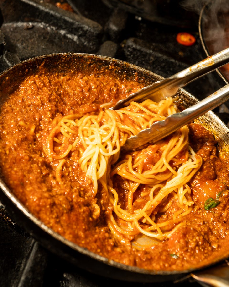 Spaghetti Bolognese tossed with tongs in the pan