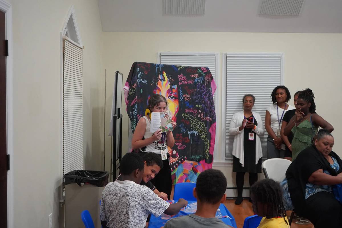 A facilitator reads a picture book aloud to kids working on a craft at an IYH workshop