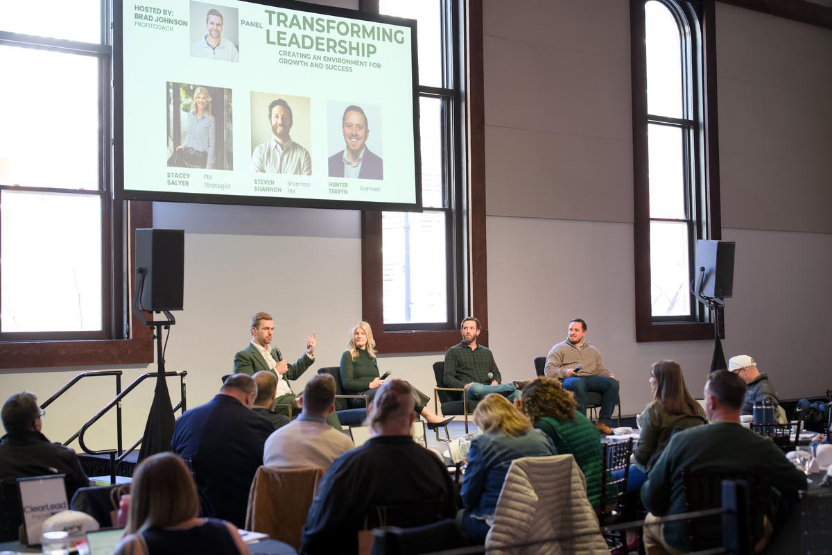 A panel on stage with the audience seated at round tables