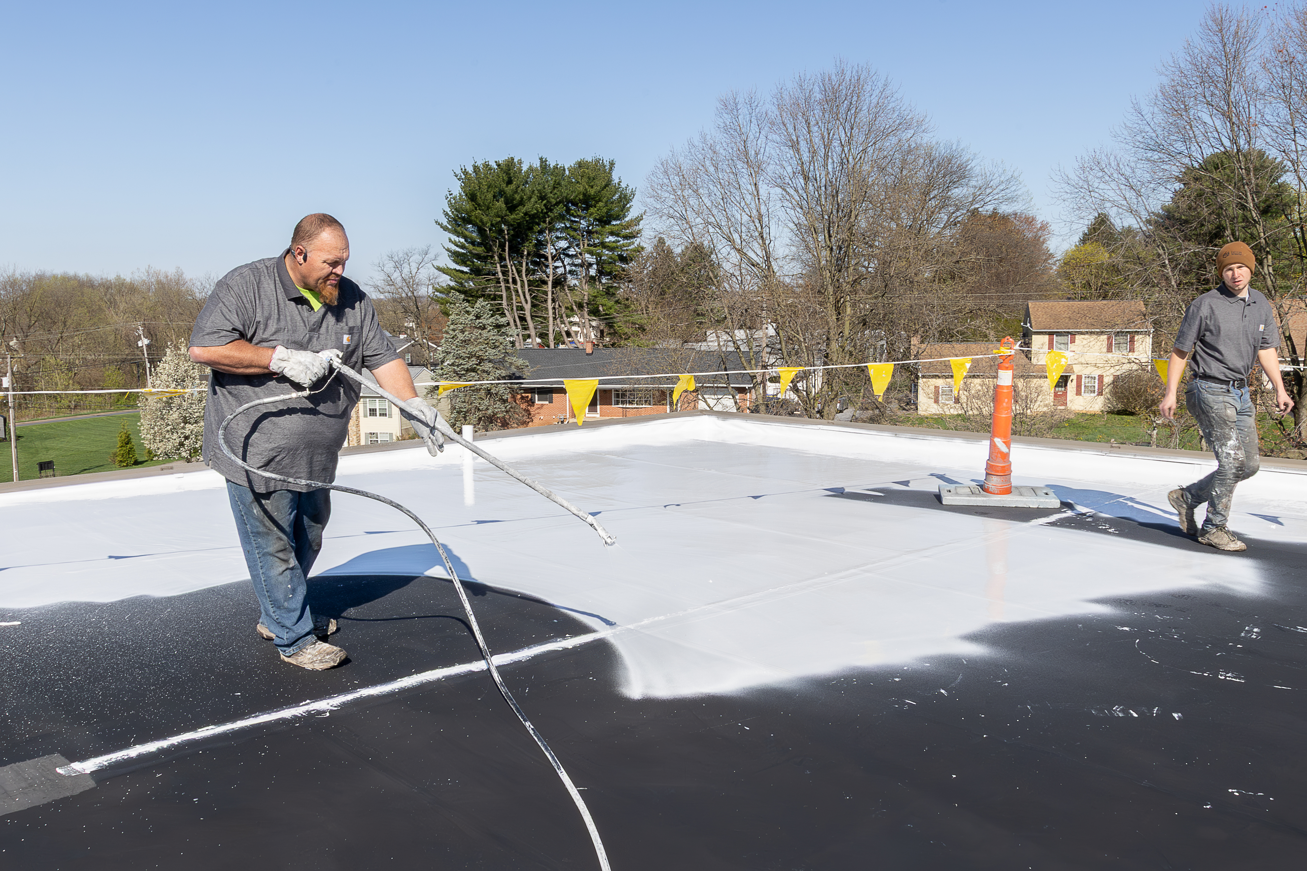 Schultz Roofing technician spray-applying white silicone coating over a black EPDM rubber roof in Middleburg, PA Schultz Roofing technician spray-applying white silicone coating over a black EPDM rubber roof in Middleburg, PA