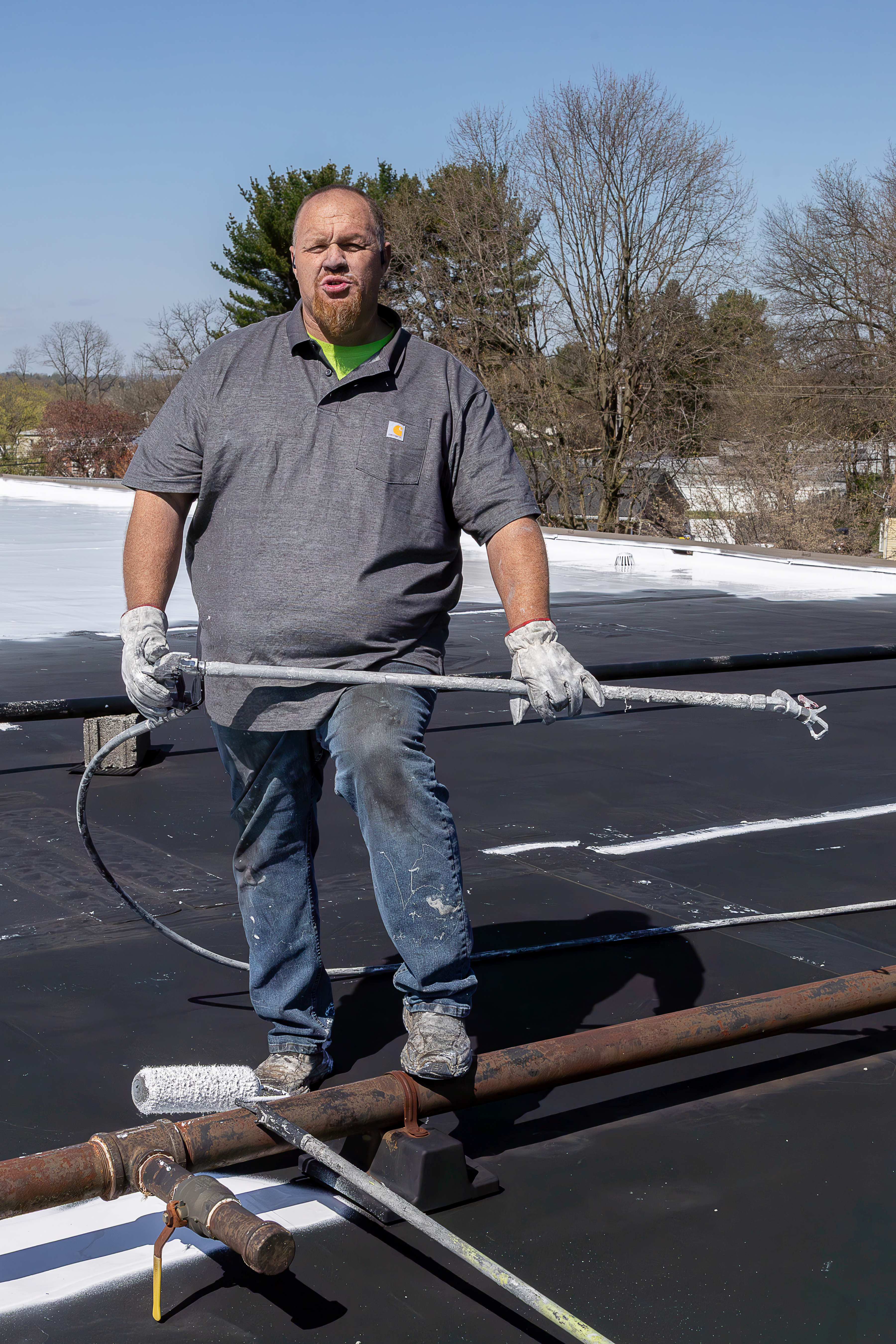 A Schultz Roofing professional applies protective coating to a flat commercial roof using specialized equipment on a clear, sunny day, demonstrating expert craftsmanship in roof maintenance and restoration. - Schultz Roofing, Inc