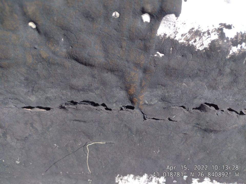 Aerial view showing a damaged flat commercial roof with visible cracks, splits, and deterioration in the roofing membrane, demonstrating the need for professional roof repair or recoating services. - Schultz Roofing, Inc