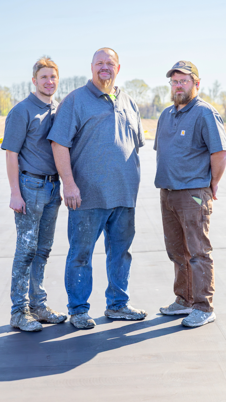 Three professional roofing contractors from Schultz Roofing, Inc. standing together on a newly completed commercial flat roof surface, showcasing their team's expertise and quality workmanship. - Schultz Roofing, Inc