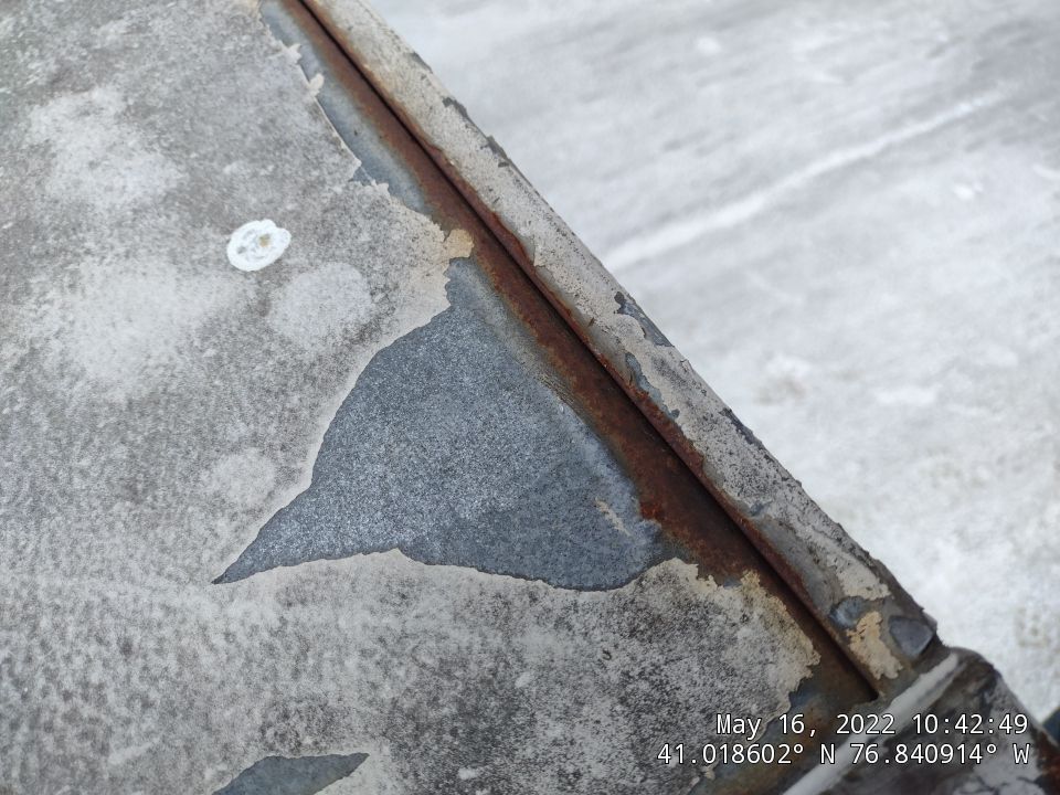 Close-up view of a deteriorating flat roof showing significant rust damage, peeling coatings, and metal corrosion around roof penetrations and seams. - Schultz Roofing, Inc