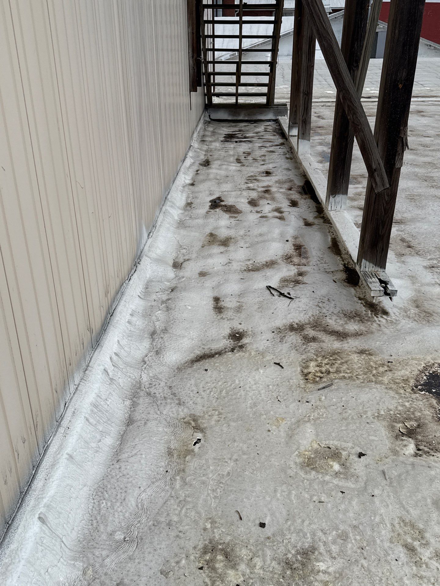 A commercial flat roof showing water damage, staining, and pooling issues on the membrane surface, with wooden support structures visible along the walkway area. - Schultz Roofing, Inc A commercial flat roof showing water damage, staining, and pooling issues on the membrane surface, with wooden support structures visible along the walkway area. - Schultz Roofing, Inc