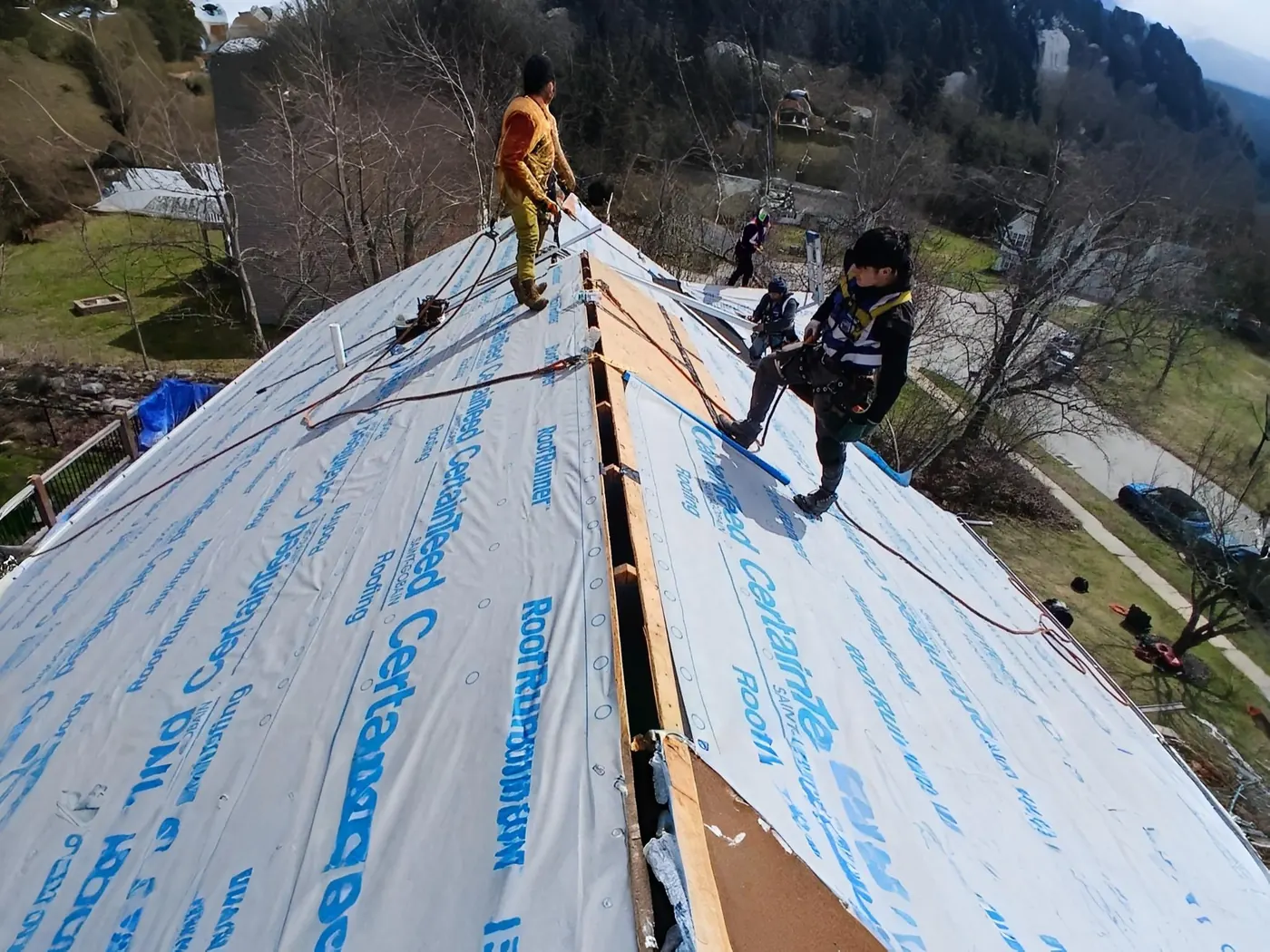 Roofing crew installing underlayment on a steep roof in South Shore Massachusetts