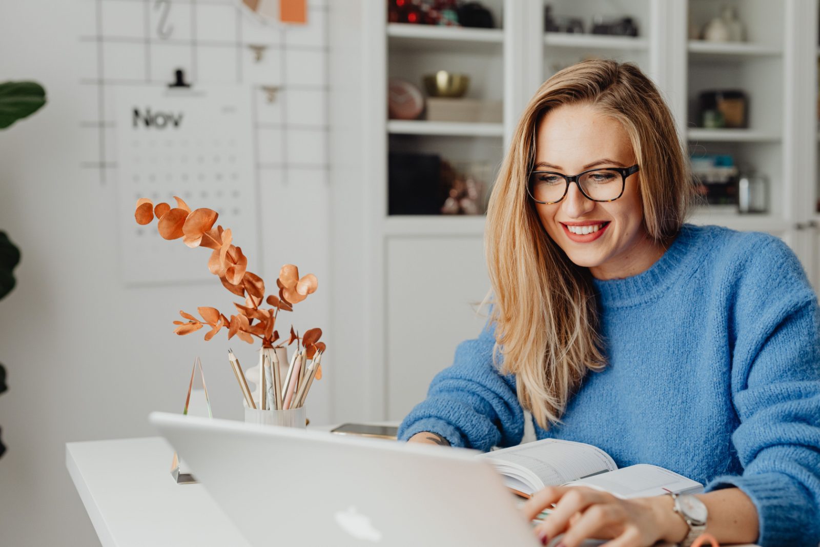 A woman smiling while using a laptop in a bright home workspace