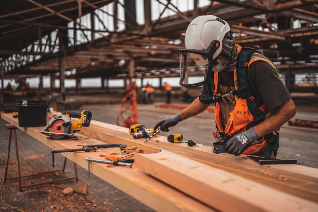 Uganda contractor in orange vest and white helmet using power tools on a timber beam — WebFast24 helps tradespeople get found online.