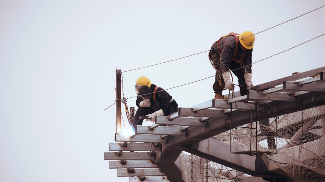 Two Uganda contractors in yellow hard hats welding steel beams at height — skilled tradespeople who win more contracts with a professional website and GBP.