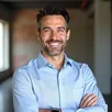 Friendly Hispanic male customer in business casual attire, smiling in an industrial warehouse with LED lighting – Juan Montealvo testimonial